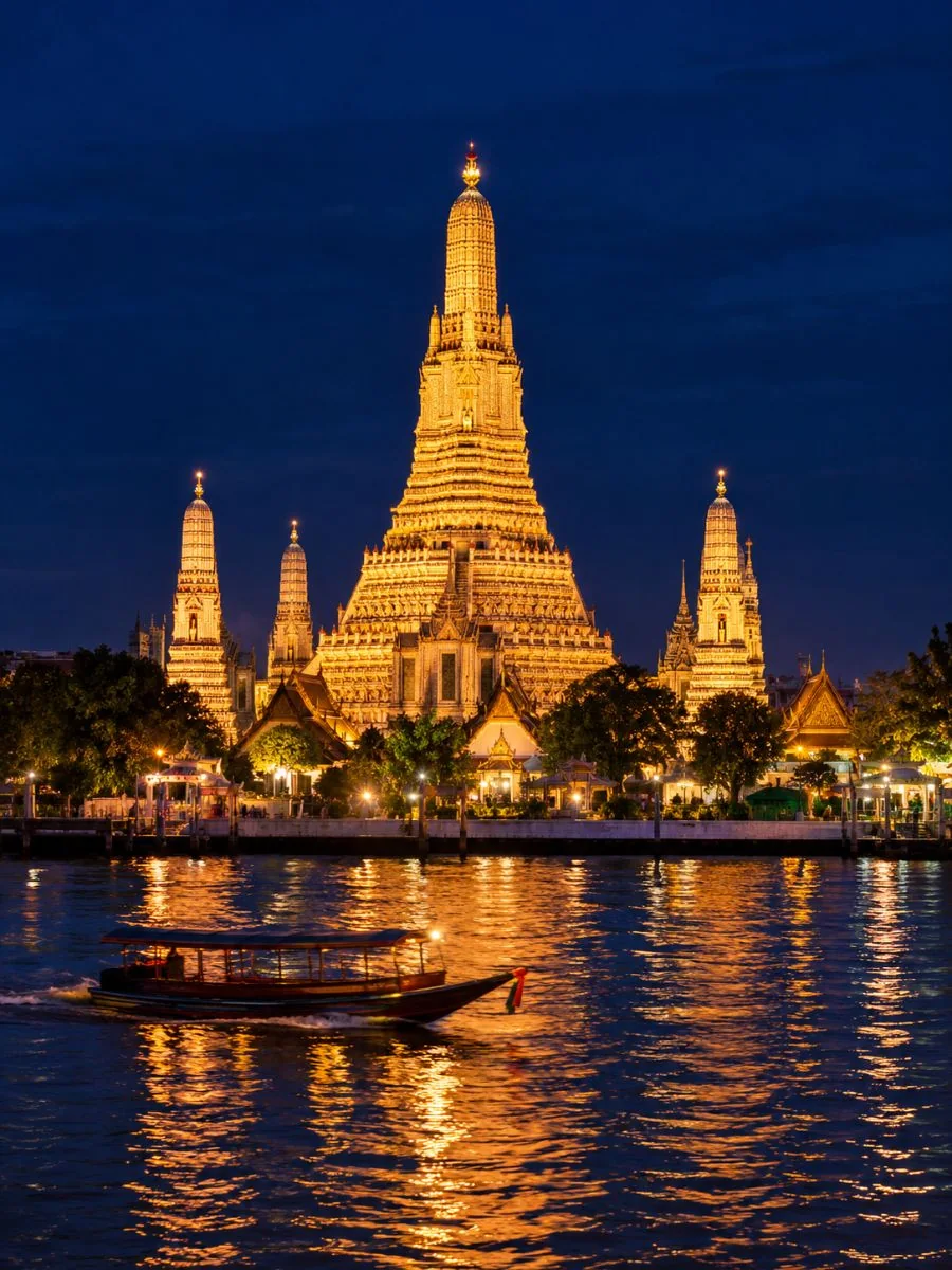 Der Stupa von Wat Arun, nachts golden beleuchtet über dem Chao Phraya Fluss, von der gegenüberliegenden Uferseite aus gesehen
